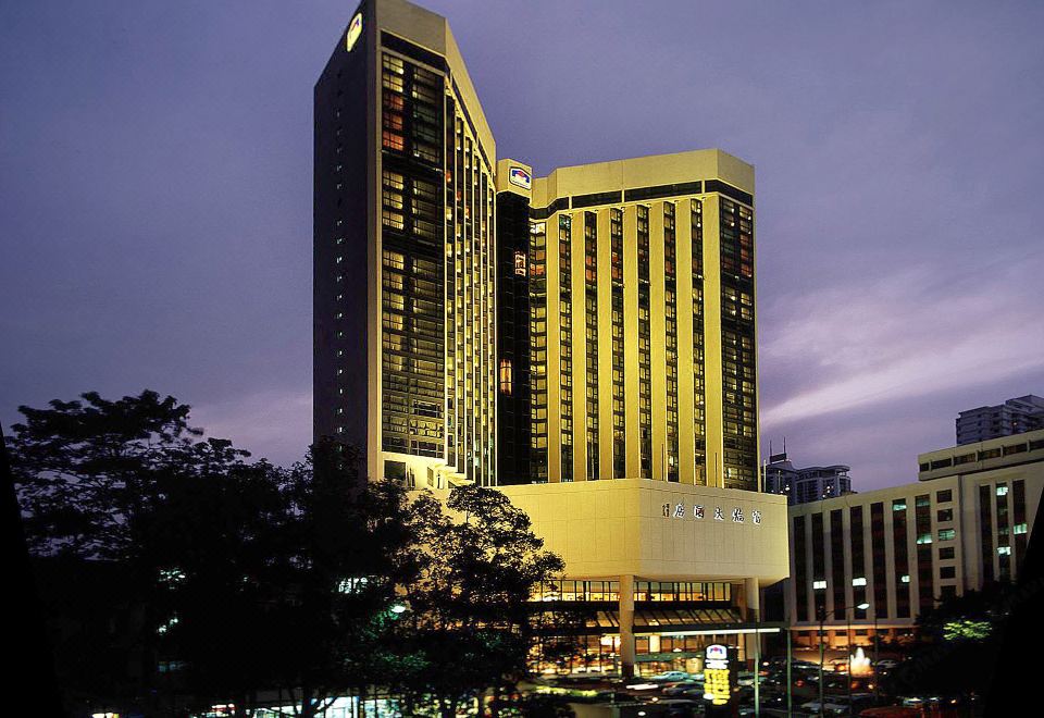At night, a brightly lit large building stands in the center, surrounded by other buildings at Best Western Felicity Hotel