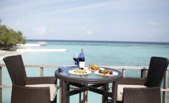 a table with a bottle of wine and snacks is set up on a balcony overlooking the ocean at Eriyadu Island Resort