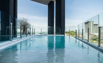 an outdoor swimming pool surrounded by a glass fence , with a view of the ocean in the background at Arize Hotel Sri Racha