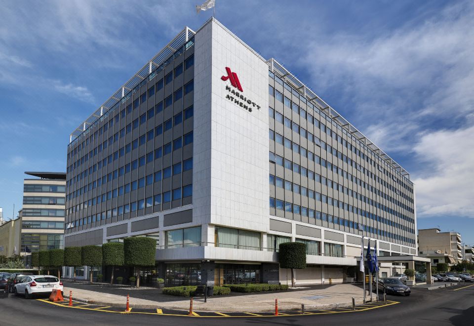a large white building with a red logo on it , situated in front of a street at Athens Marriott Hotel
