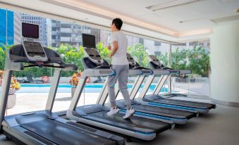 A man is running on a treadmill in an indoor gym while another person stands next to him at Novotel Century Hong Kong