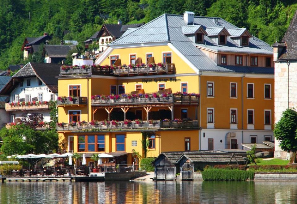 a yellow building with balconies and windows is situated on the banks of a river , surrounded by trees at Seehotel Gruner Baum