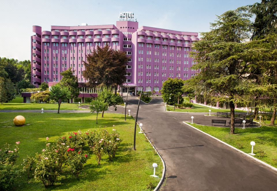 a large pink hotel building with a large sign on top , surrounded by a park - like setting at Hotel Da Vinci