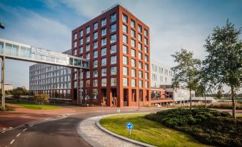 a tall red brick building surrounded by grass and trees , with a car parked nearby at Fletcher Wellness-Hotel Leiden