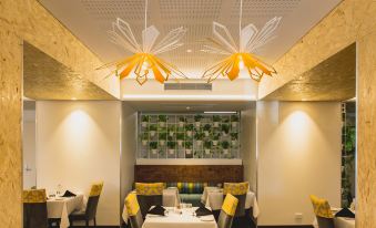 a modern dining room with yellow and white accents , including two hanging light fixtures , a bar area , and tables set for diners at Metro Hotel Perth
