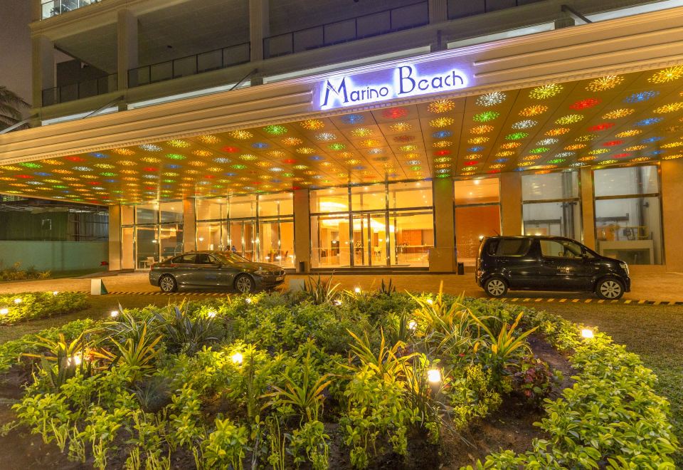"a brightly lit hotel entrance with the name "" manalo beach "" on it , surrounded by greenery and cars parked outside" at Marino Beach Colombo