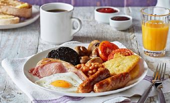 a delicious breakfast plate with various food items , including bacon , eggs , mushrooms , and toast , accompanied by coffee and jam at Premier Inn Derby East