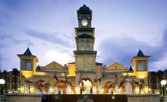 a large building with a clock tower in the center , surrounded by trees and other buildings at Gold Reef City Theme Park Hotel