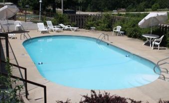 an outdoor swimming pool surrounded by a patio area , with several lounge chairs and umbrellas placed around the pool at Rocky River Inn