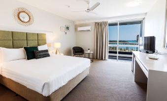 a hotel room with a large bed , a tv , and a balcony overlooking the ocean at Greenmount Beach House