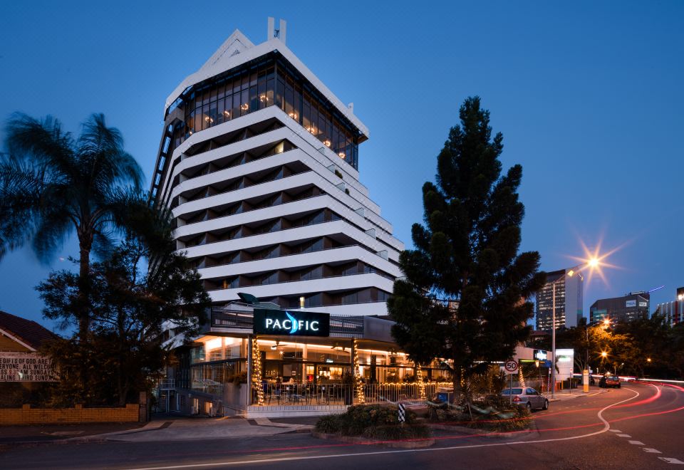 a tall building with a white facade and blue lights is the pacific hotel , located in a city street at Mercure Brisbane Spring Hill