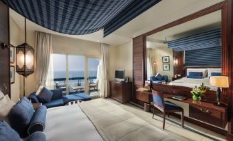 a luxurious hotel room with a large bed , desk , and balcony offering a panoramic view of the ocean at Ajman Hotel by Blazon Hotels