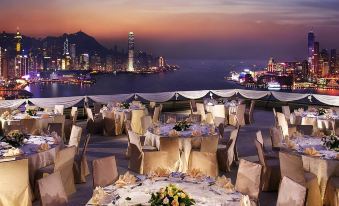 A dinner table is set in the middle, with a backdrop of the city and water at dusk at Harbour Grand Hong Kong