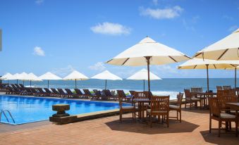 a large swimming pool surrounded by lounge chairs and umbrellas , with the ocean visible in the background at Galle Face Hotel