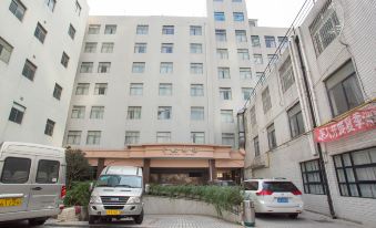 The entrance to a hotel is depicted with cars parked in front and an adjacent apartment building at Yuhang Hotel