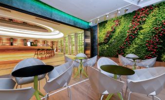 The restaurant features large windows, with plants on both sides, and an interior design that includes walls and tables at OASIS AVENUE – A GDH HOTEL