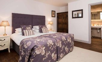 a bedroom with a large bed covered in purple and white floral sheets , accompanied by a nightstand and lamp at The Lamb at Angmering