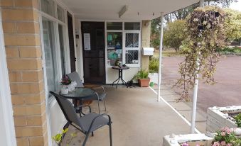 a covered porch with a table , chairs , and potted plants , providing a comfortable outdoor seating area at Emu Point Motel