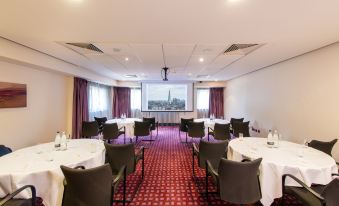 a conference room with a red and white checkered carpet , tables with chairs and windows , and a projector screen at DoubleTree by Hilton London Heathrow Airport