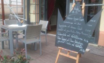 a blackboard with white chalk writing is displayed in front of a wooden table and chairs at LUDWIGS