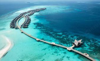 a long pier leads to a row of overwater bungalows in the middle of a turquoise ocean at Joali Maldives
