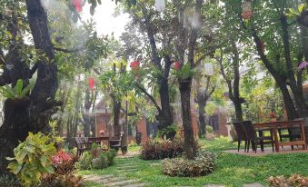 a lush green garden with trees , grass , and flowers , as well as a brick building in the background at Khum Wang Nuea Villa