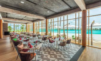 a modern , open - air restaurant with large windows offering views of the ocean and a dining area with wicker chairs and tables at Hard Rock Hotel Maldives