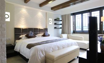The room features a large bed with a wooden headboard, set in an all-white space with a brick accent wall at West Lake Teavilla