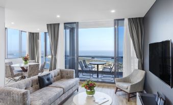 a spacious living room with a couch , chair , and dining table overlooking the ocean from a balcony at Meriton Suites Southport