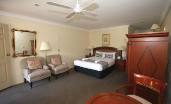 a large bed with a white and gray striped blanket is in the center of a room with two chairs , a table , and a fan at Picton Valley Motel Australia