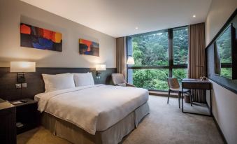 a hotel room with a large bed , a desk , and a window overlooking a forest at Platinum Hotel