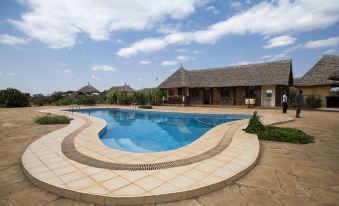 a large outdoor swimming pool surrounded by a grassy field , with several lounge chairs and umbrellas placed around the pool area at AA Lodge Amboseli