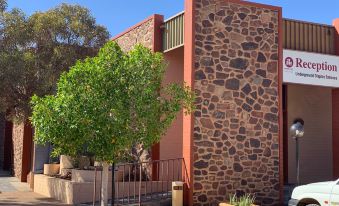 a stone building with a red roof , surrounded by trees and potted plants on the ground at Desert Cave Hotel