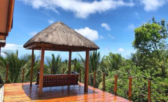 a wooden deck with a thatched roof structure overlooking a tropical landscape under a blue sky at Volcano House