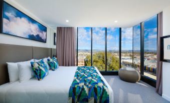 a large bed with a colorful blanket is situated in a bedroom with a view of the city at Mantra Albury Hotel