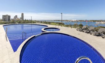 a large outdoor swimming pool surrounded by grass and trees , with a view of the ocean in the background at Meriton Suites Southport