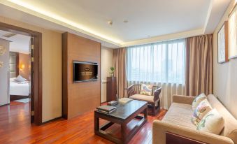 A contemporary living room with expansive windows features a central couch and table, while facing an open kitchen that includes a dining area and breakfast bar at Byland World Hotel (Yiwu International Trade City)