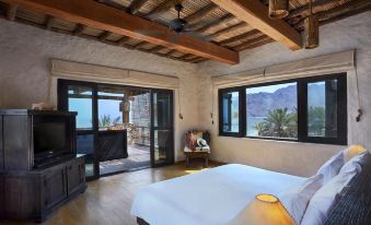 a large bed with a white comforter is in a room with wooden floors and a sliding glass door leading to a balcony at Six Senses Zighy Bay