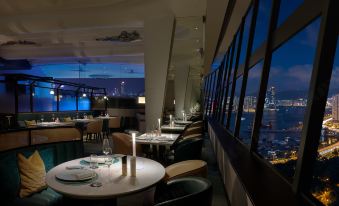 The restaurant on an upper floor offers a scenic view of the city at night, with tables and chairs for dining at The Park Lane Hong Kong a Pullman Hotel