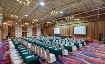 a large conference room with rows of tables and chairs , multiple screens , and chandeliers hanging from the ceiling at Paradise Hotel