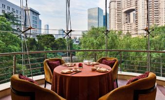 There is a dining room with a table and chairs, featuring large windows that provide a view of the outside at Grand Millennium Shanghai HongQiao