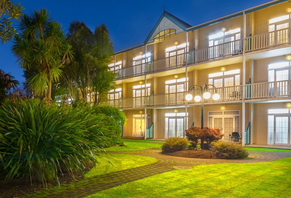 a large building with multiple balconies and a lush green lawn in front of it at Wairakei Resort Taupo