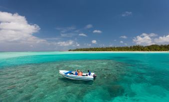 a group of people are enjoying a boat ride in the ocean , surrounded by clear blue water and a white sandy beach at Meeru Maldives Resort Island