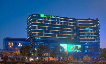 At night, there is a hotel in the foreground and an illuminated building in the background at Holiday Inn Express Hangzhou East Station