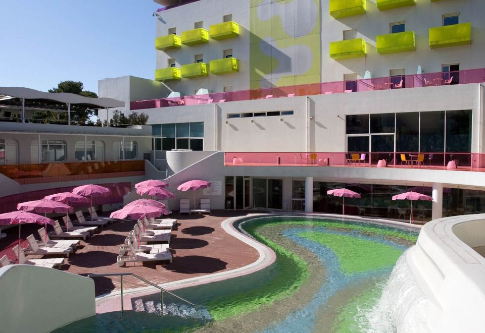 a modern hotel with a large swimming pool , umbrellas , and pink umbrellas in front of the building at Semiramis