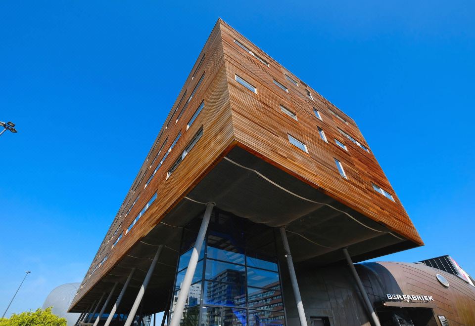 a modern building with a large glass window and wooden exterior is shown against a blue sky at Leonardo Hotel Almere City Center