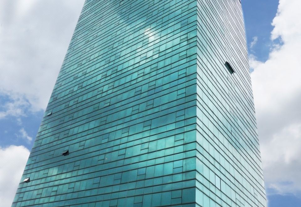 a tall , modern building with a glass facade is situated under a cloudy blue sky at Bay Hotel Srinakarin