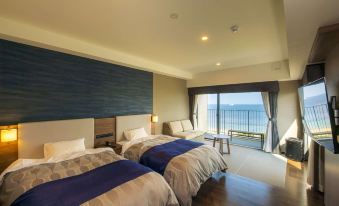 a room with two beds , one on each side of the room , and a view of the ocean outside at Rex Hotel Beppu