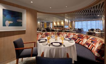 a restaurant with a round table set for dinner and chairs , surrounded by windows and artwork on the wall at Hotel Royal