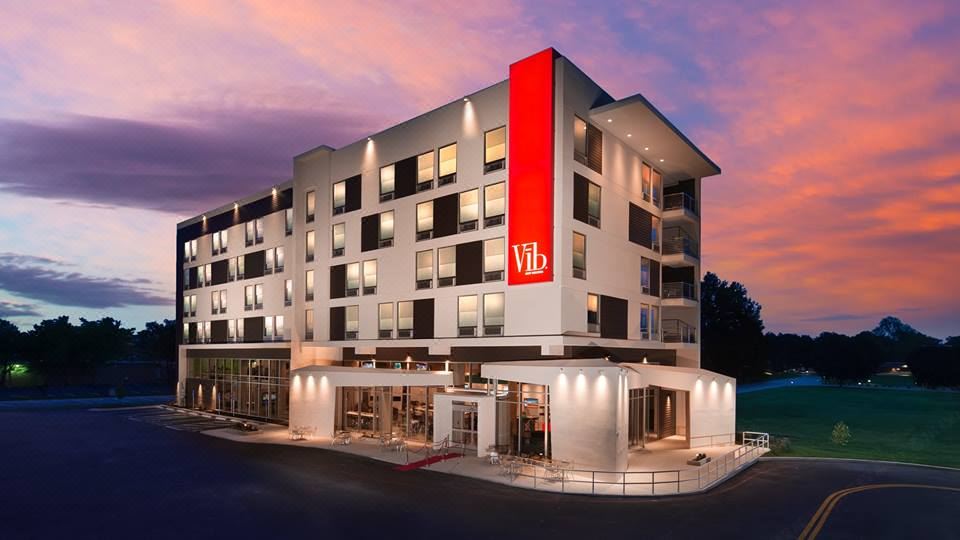 "a modern hotel with a red sign that reads "" viiis "" in front of it , surrounded by trees and a sunset" at Best Western Plus Executive Residency Austin